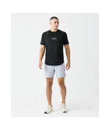 A man modeling a black short-sleeve athletic t-shirt with white text on the chest, paired with light gray running shorts and white sneakers, against a plain white studio background.